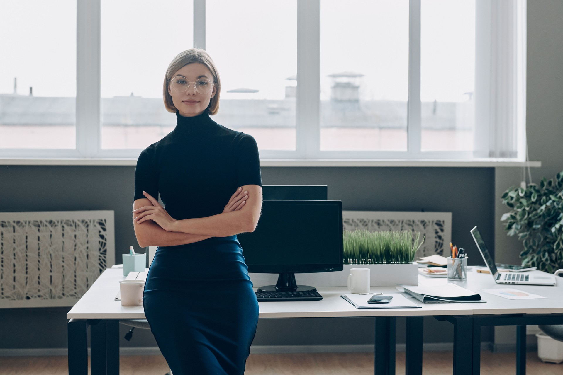 Confident businesswoman keeping arms crossed while leaning at the office desk
