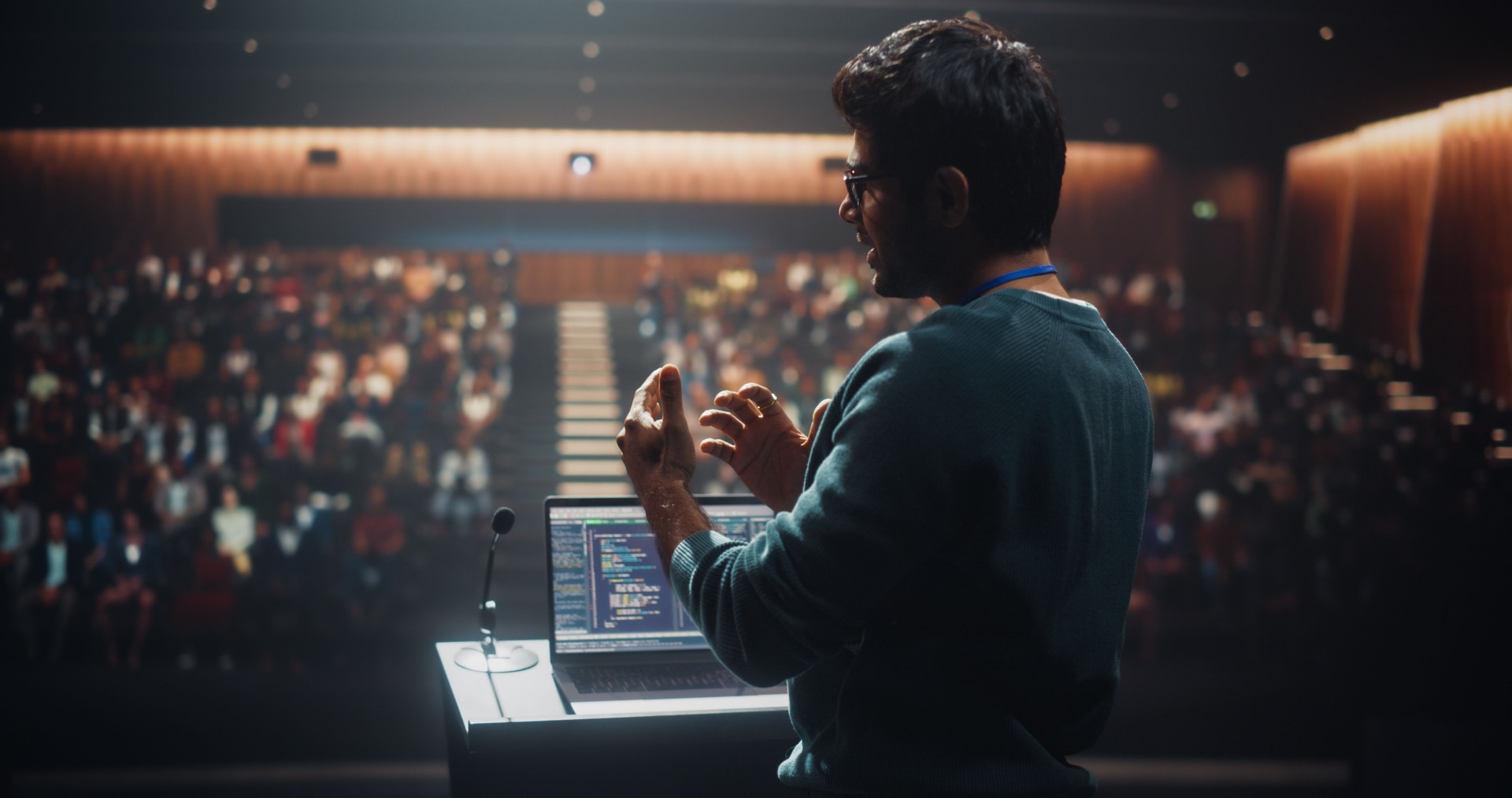 Portrait of a Young Speaker Standing on a Conference Stage. Technology Startup Founder Using a Laptop Computer, Speaking About Software Integration at a Business Meeting with Professional Audience